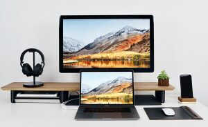 Macbook & iMac on computer desktop next with iPhone and headphones nearby